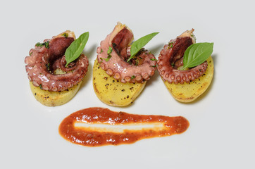 Platillo gourmet de pulpo con especias en una cama de patatas y salsa picante, en un plato blanco con mantel, platillo mexicano del mar