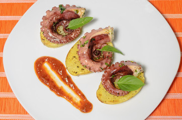 Platillo gourmet de pulpo con especias en una cama de patatas y salsa picante, en un plato blanco con mantel, platillo mexicano del mar
