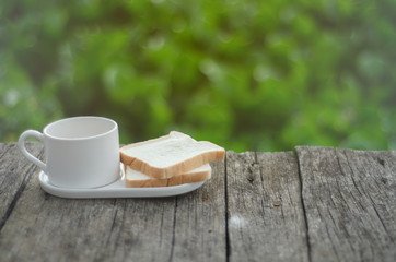 White bread and glass placed on the table in the morning.On the breakfast table there was a glass of coffee and a plate of bread.Breakfast set on wooden floor in the morning.