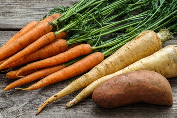 Close up of a bundle of carrots, parsnip and sweet potato on a rustic wooden table. Concept for root vegetable, organic raw food, farming and harvest.