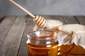Pouring aromatic honey into jar, closeup. Honey in glass jars and honeycombs wax on wooden background. Wooden stick , instruments