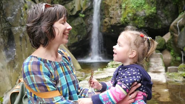 Mother and little child daughter kissing hugging on nature near waterfall