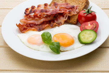 Fried eggs with bacon on the wooden table.