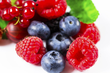 Close-up arrangement mixed, assorted berries including blackberries, strawberry, blueberry, raspberries and fresh leaf on white