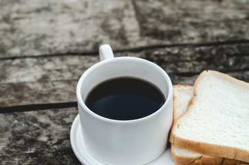 White bread and glass placed on the table in the morning.On the breakfast table there was a glass of coffee and a plate of bread.Breakfast set on wooden floor in the morning.