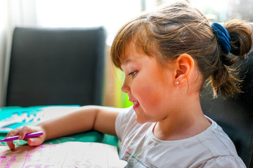 A young girl writing letters with a pink pen and paper