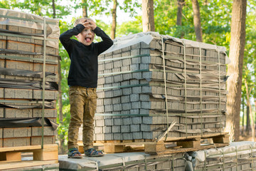 A small boy grabbed his head and stood on a pallet with a building tile. The concept of blockage, the decline of forces, the ambiguity of what to do, depression.