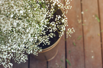 Bouquet of tiny gypsophila flowers in gold vintage metal bucket. beautiful baby's breath on wooden background. Top view, copy space