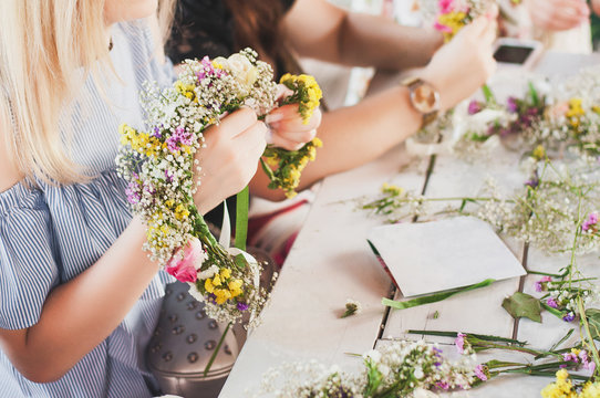 Workshop florist, making bouquets and flower arrangements. Girl makes wreath at head. Process of weaving a wreath with herbs and flowers. Lesson of florists close-up. Copy space