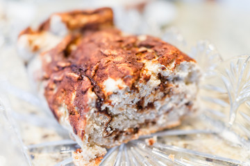 Closeup of cut golden baked whole cinnamon roll cake, or babka pastry bread in crystal glass dish on table holiday