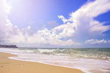 foaming wave gently envelops along a sandy beach, on a background of blue sky with Cumulus clouds.