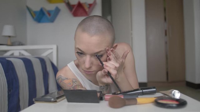 TATTOOED GIRL with shaved head applies EYE MAKE UP