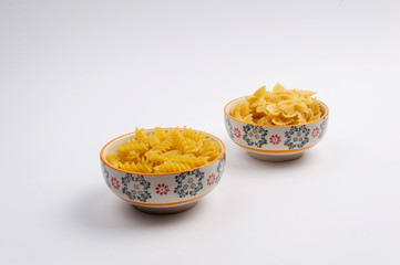 Two ceramic bowls full of farfalle pasta and rotini on white background
