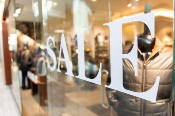 Closeup of Sale sign on clothes, clothing, apparel retail store, shop window in shopping mall
