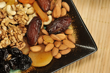 Dried fruits and nuts on a square plate. The background is a napkin made of bamboo. View from above. Close-up. Macro photography.