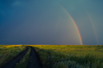 Double rainbow after rain on the background of storm clouds.Road in field.
