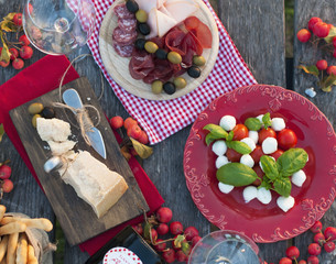Italian picnic with red wine, Parmesan, ham, caprese salad and olives. Lunch in the open air and wooden table. Traditional snacks
