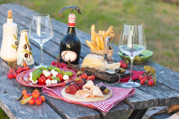 Italian picnic with red wine, Parmesan, ham, caprese salad and olives. Lunch in the open air and wooden table. Traditional snacks