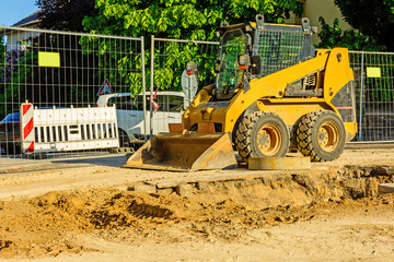 Orange dredger at a building site in the city. Construction of sewerage in the area. Parked work machines on the road. Bulldozer on site. Dropped road.