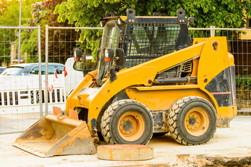 Orange dredger at a building site in the city. Construction of sewerage in the area. Parked work machines on the road. Bulldozer on site. Dropped road.