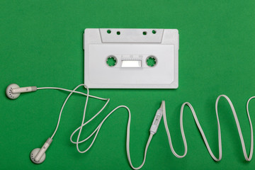 white audio cassette and white headphones on green background