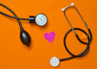 Cardiological concept. Medical monometer, stethoscope, decorative heart on a yellow background. Top...