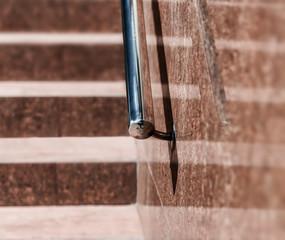 Stone granite stairs steps background with metallic aluminium handle. Red brown modern stairs