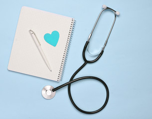 Notepad with pen, decorative heart, stethoscope on pink pastel background, medical concept, top...