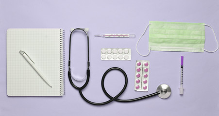 Medical equipment on a pink pastel background. Blisters pills, notepad, stethoscope, thermometer,...