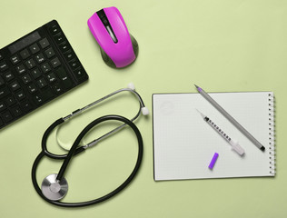 Workplace of a modern doctor. Keyboard, wireless mouse, notebook, stethoscope, syringe on a blue pastel background. top view, minimalist trend.