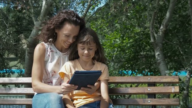 Happy family on the Internet. Mother with daughter with gadget in the park.
