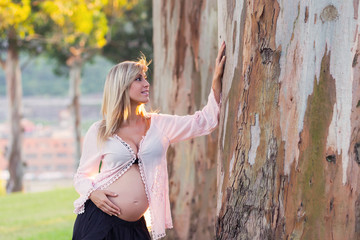 Blonde pregnant woman in a park, with pleasure expecting baby. Outdoors, on a sunny day. Second trimester pregnancy.