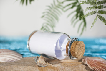 Stranded bottle message note paper with cork on a beautiful holiday beach on the ocean sea with palms and shells