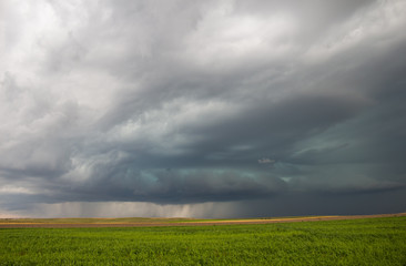 Fototapeta premium An approaching severe storm emits a strange green glow in the sky. Heavy rain is seen under the cloud base.