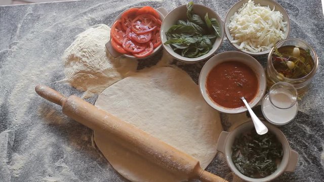 Raw dough for pizza with ingredients and spices on table