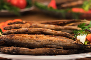 Whole fried fish, stacked on a plate with slices of sweet pepper, tomatoes and cheese.
