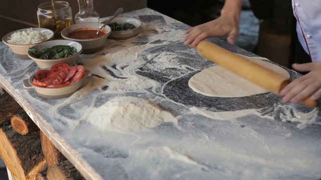 Chef in the restaurant rolls out the dough for traditional pizza