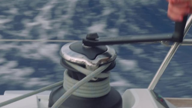 Close up view of man's hand twisting rope on winch of sailing yacht.