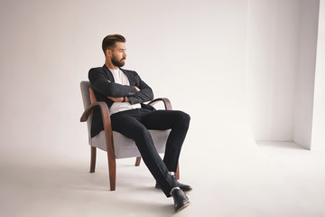 Indoor portrait of handsome young male lawyer with thick beard and trendy hairstyle sitting...