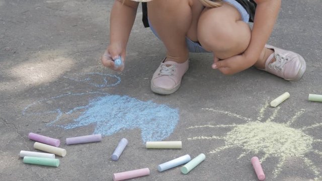A little girl draws chalk on the asphalt. The child draws the sun in the park.