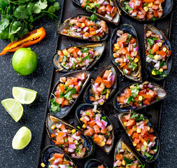 PERUVIAN FOOD. Choros a la chalaca. Big mussels, choros zapatos seasoned with purple onion, tomatoes, corn and lemon. Top view, black background. Traditional peruvian dish