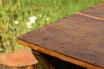 Raindrops on a wooden table in the garden. A means to protect outdoor furniture from the wood from rain and moisture. Water-wiping properties of impregnation based on wax