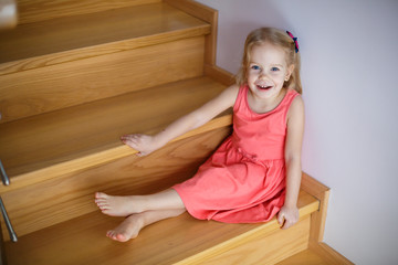 Portrait of little cute girl smiling on stairs in cozy room