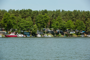 Fototapeta na wymiar Camping Site with private Boats situated under Trees on a Lake on a sunny Day