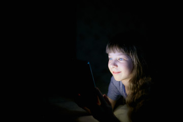little girl with a tablet on the bed at night