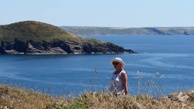 Lady walking back to camera on coast path, over looking St Brides Bay on a summers day.