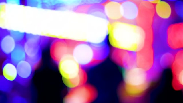 Panning over defocused funny atmosphere at the amusement park in megapolis with multiple colorful lights