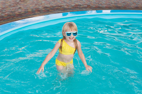 Little girl in a yellow swimsuit and sunglasses is swimming and jumping to swimming pool at resort. Summer fun in the pool.  - Powered by Adobe