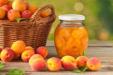 Apricot compote in a glass jar and a bunch of mature apricots in a basket on a wooden table. Sweet and healthy dessert.