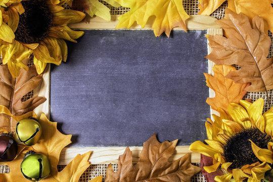 blank chalkboard on burlap framed with autumn leaves yellow sunflowers and fall colored bells with copy space in the middle